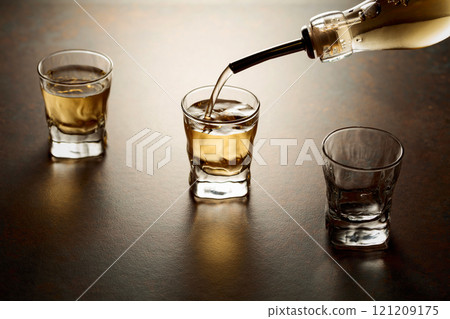 Whiskey pour from a bottle into a small glasses. 121209175