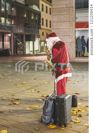 Santa Claus playing saxophone on a city street. Concept of festive street performance, holiday entertainment Santa Claus playing saxophone on a city street. Concept of festive street performance, holiday entertainment 121209414