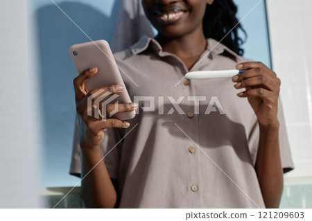 Cropped shot of happy young African American woman holding express pregnancy test with reassuring result while text messaging on mobile phone in bathroom, copy space Cropped shot of happy young African American woman holding express pregnancy test with reassuring result while text messaging on mobile phone in bathroom, copy space 121209603