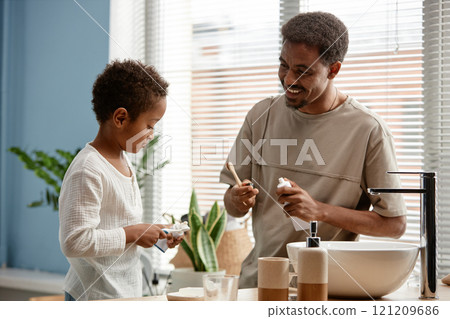 Medium shot of happy father looking at little son with affectionate smile while brushing teeth together in bathroom on Sunday morning Medium shot of happy father looking at little son with affectionate smile while brushing teeth together in bathroom on Sunday morning 121209686