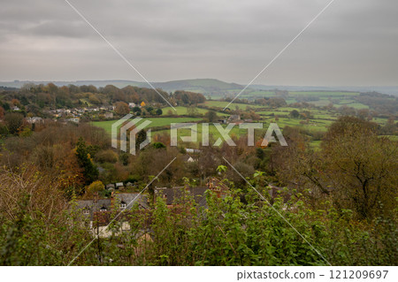 View of the English countryside near Shaftesbury, Dorset with fields, trees, hills and a farm with sheep. 121209697