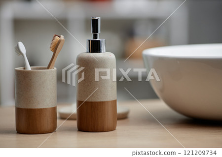 Background shot of soap dispenser and ceramic toothbrush holder placed on bathroom vanity near sink, zero waste concept, copy space 121209734