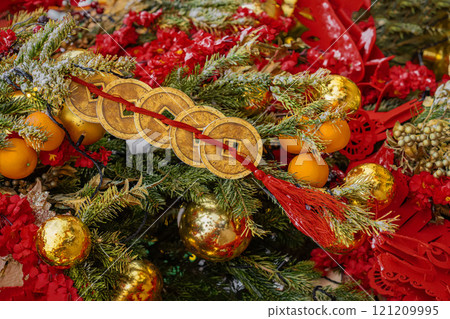 Festive arrangement of red and gold ornaments and traditional Chinese coins tied with red ribbon, vibrant holiday decor 121209995