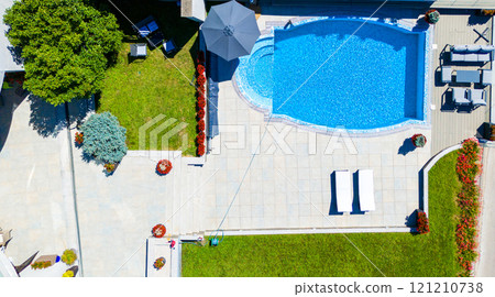 Aerial view of a luxury swimming pool with clear blue water, a surrounding patio, and green lawn. Concept of outdoor summer relaxation and modern backyard design 121210738