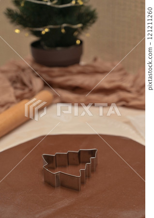 Christmas homemade baking, brown cocoa dough for baking gingerbread with tree shaped cutter, rolling pin on the table, blurred background 121211260