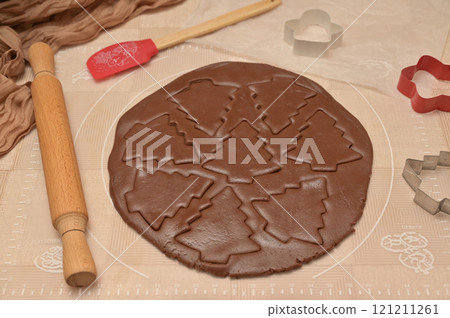Christmas homemade baking, brown cocoa dough cut into tree shapes for baking gingerbread, cutter, rolling pin, spatula on the table 121211261