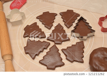 Christmas homemade baking, brown cocoa dough cut into tree shapes for baking gingerbread, cutter, rolling pin, spatula on the table 121211262