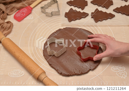 Christmas homemade baking, woman hand cuts out dough for baking gingerbread, cutter, rolling pin, spatula on the table 121211264