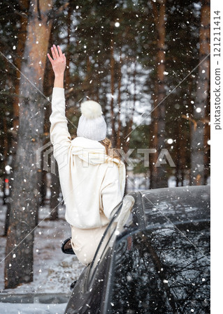 Young woman in woolen white hat have a fun in black car. Winter travel, snow-covered trees in the forest. Snowy weather. Young woman in woolen white hat have a fun in black car. Winter travel, snow-covered trees in the forest. Snowy weather. 121211414