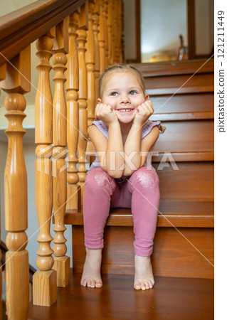 Happy little girl is sitting alone on stairs at home. Dangerous situation at home. Child safety concept.  121211449