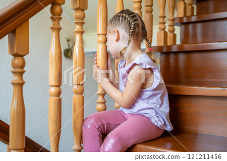 Little girl is sitting on stairs at home. Dangerous situation at home. Child safety concept. Little girl is sitting on stairs at home. Dangerous situation at home. Child safety concept. 121211456