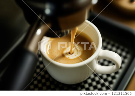Close-up of rich espresso coffee pouring into a white ceramic cup from coffee machine 121211565