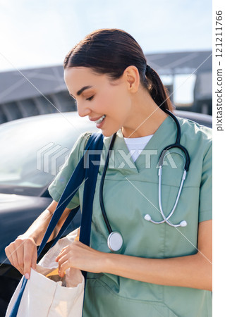 Smiling young nurse with a bag on her shoulder near the car Smiling young nurse with a bag on her shoulder near the car 121211766
