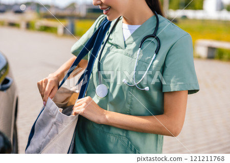 Smiling young nurse with a bag on her shoulder near the car Smiling young nurse with a bag on her shoulder near the car 121211768