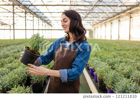 Dark-haired young woman standing in a greenhouse with a potted plant in hands 121211810