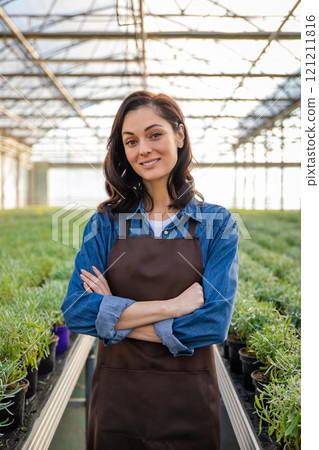 Dark-haired young woman in apron in a greenhouse 121211816