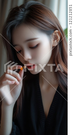 A sick young Asian girl is holding a vitamin capsule close to her lips, preparing to take a dietary supplement for skin and hair health 121212851