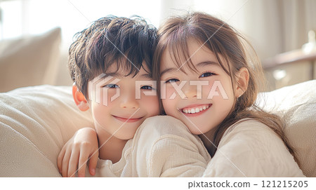 Young brother and sister sitting close together on a sofa in a bright room 121215205