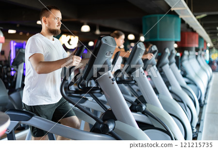 Young man working out on elliptical machine 121215735