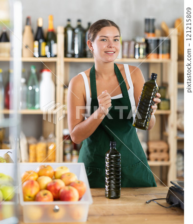 Young woman seller offering olive oil in grocery 121215809