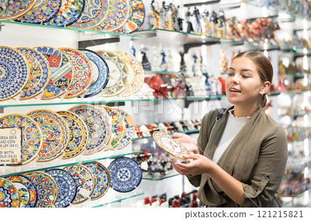 Portrait of happy woman near souvenirs shelves in store 121215821