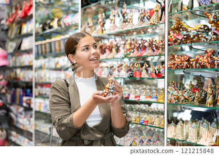 Happy female tourist chooses Spanish handmade souvenirs - figurines of flamenco dancers displayed in shop for sale 121215848
