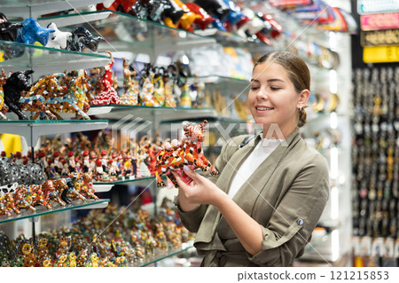 Cheerful female tourist choosing colorful bull statuette at tourist shop 121215853