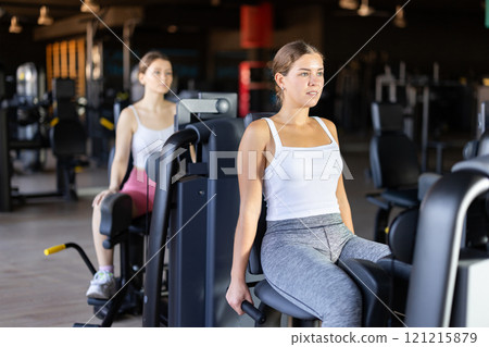 Slender athletic girl work out muscles of legs and thighs on simulator in fitness club Slender athletic girl work out muscles of legs and thighs on simulator in fitness club 121215879
