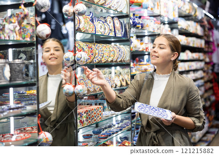 Cheerful female tourist choosing gift decorative plates at tourist shop 121215882