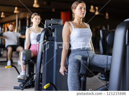 Slender athletic girl work out muscles of legs and thighs on simulator in fitness club Slender athletic girl work out muscles of legs and thighs on simulator in fitness club 121215896