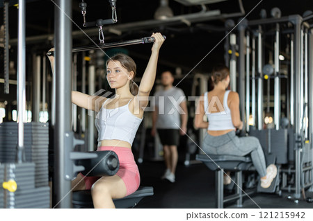 Slender athletic woman work out muscles of hands on cable crossover machine in fitness club Slender athletic woman work out muscles of hands on cable crossover machine in fitness club 121215942