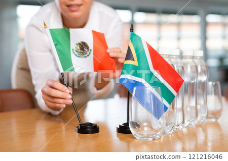 Little flag of South Africa on table and flag of Mexico put next to it by young woman Little flag of South Africa on table and flag of Mexico put next to it by young woman 121216046