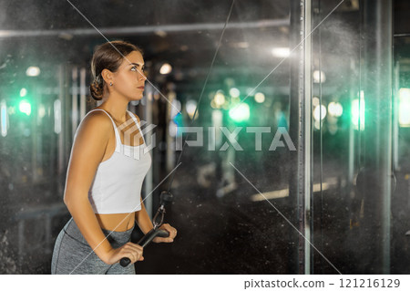 Young woman exercising her arms on cable machine 121216129
