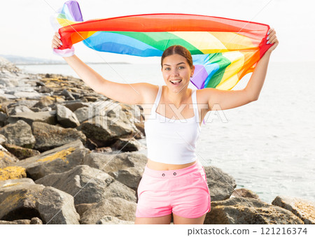 Young woman on coast posing with LGBT flag 121216374
