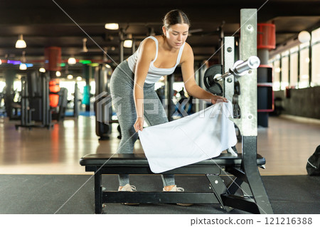 Girl lays white towel on bench, covers simulator for individual training. Girl lays white towel on bench, covers simulator for individual training. 121216388