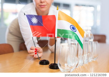 Woman secretary prepares an office for negotiations - she places flags of Taiwan and India table 121216399