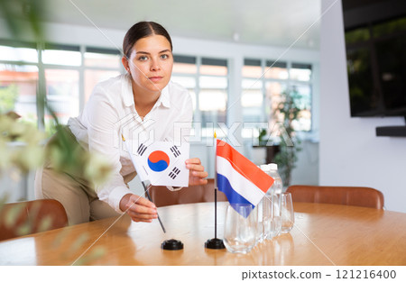 Young woman putting South Korea and Netherlands flags on table in office Young woman putting South Korea and Netherlands flags on table in office 121216400