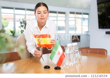 Woman secretary prepares an office for negotiations - she places flags of Spain and Iran table Woman secretary prepares an office for negotiations - she places flags of Spain and Iran table 121216534