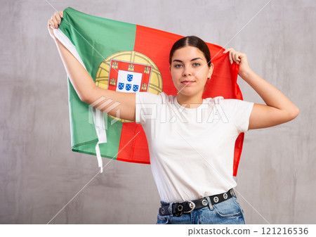 Serious young woman holding national flag of Portugal against gray wall background Serious young woman holding national flag of Portugal against gray wall background 121216536