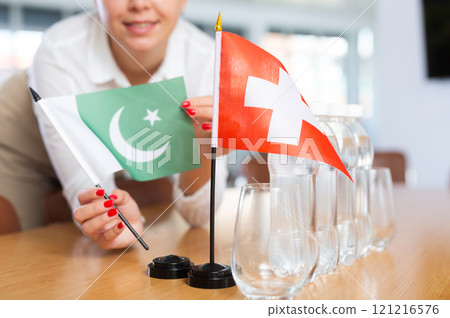 Young woman putting flags of Pakistan and Switzerland on table in office 121216576