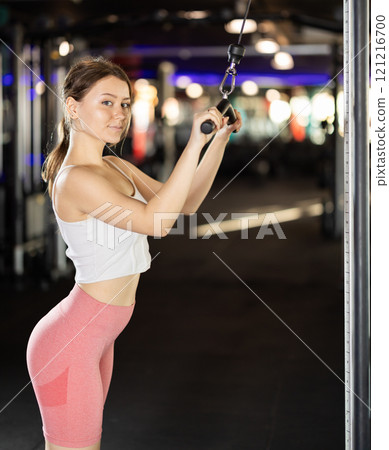 Slender athletic woman work out muscles of hands on cable crossover machine in fitness club Slender athletic woman work out muscles of hands on cable crossover machine in fitness club 121216700