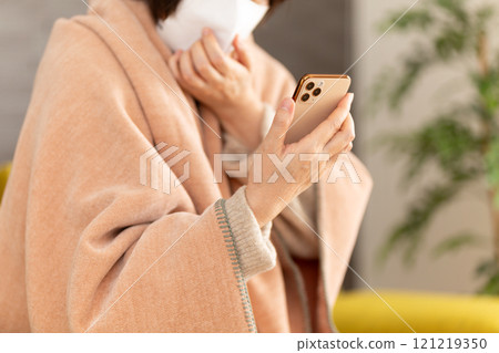 A middle-aged to senior woman wearing a mask and looking at her smartphone in a room A middle-aged to senior woman wearing a mask and looking at her smartphone in a room 121219350