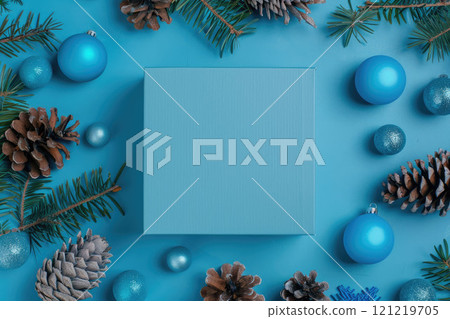 Cardboard blank gift box close up in blue colors. Blue balls, cones and fir tree twigs around. Christmas flat lay. 121219705