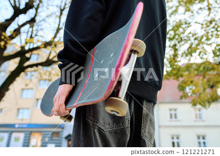 Skateboarder holding worn skateboard walks at street 121221271