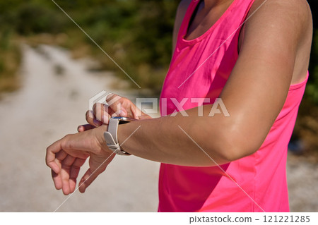 Female athlete using fitness watch while running on sunny day 121221285
