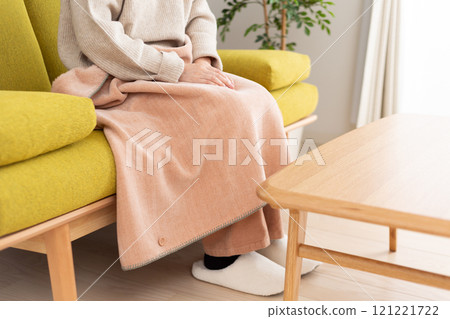 Middle-aged to senior woman with a blanket on her knees in a winter room 121221722