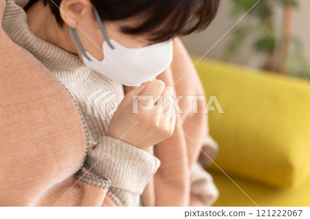 Middle-aged to senior woman coughing in a winter room Middle-aged to senior woman coughing in a winter room 121222067