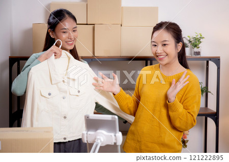 Two young asian woman live online clothing store while showing clothing with tablet on social. 121222895