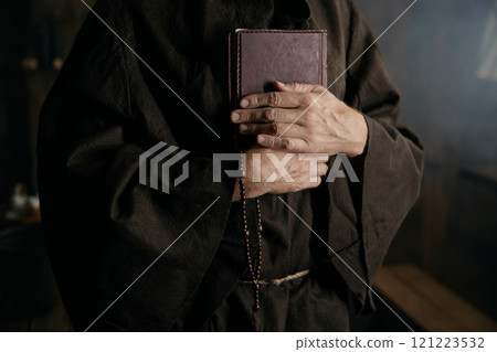 Priest holding closed bible book and rosary beads in hands closeup Priest holding closed bible book and rosary beads in hands closeup 121223532