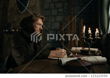 Medieval monk chronicler writing ancient manuscript under candlelight 121223550